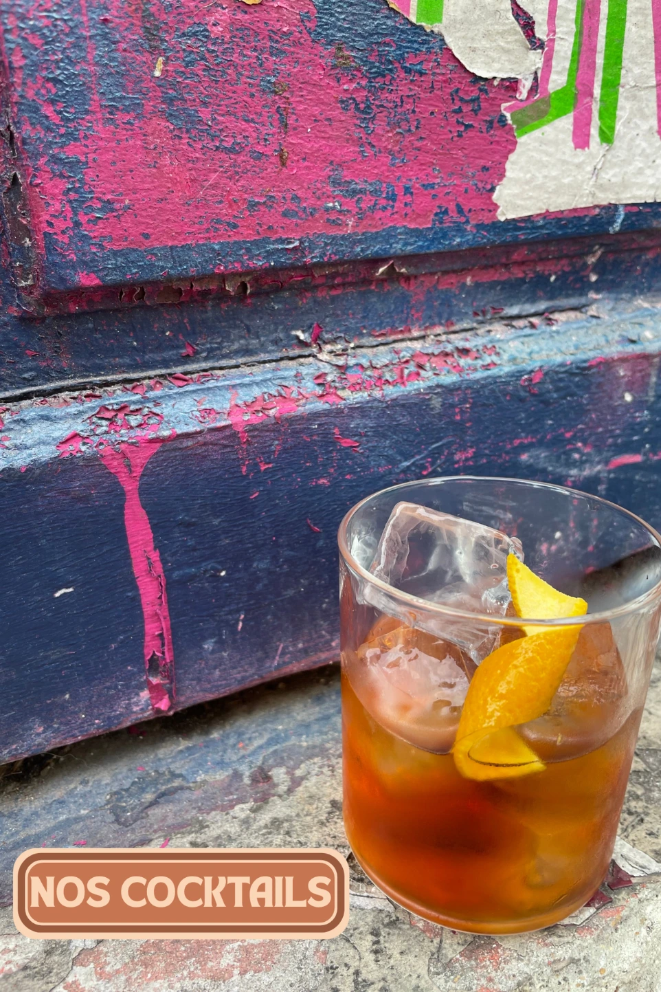 Cocktails du Café des Délices : cocktail ambré sur glace et zeste d'orange, devant un mur graffé de Belleville