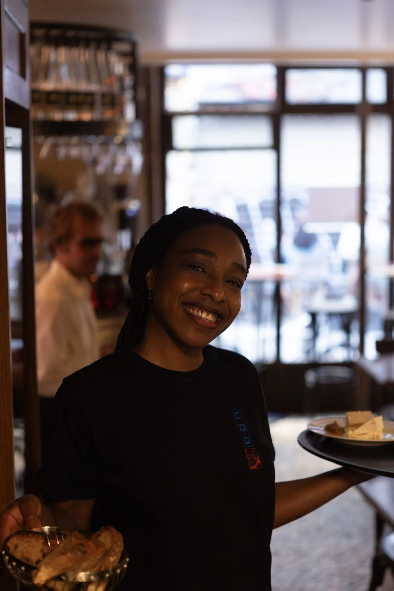 Serveuse souriante en salle, assiettes à la main, au Café des Délices