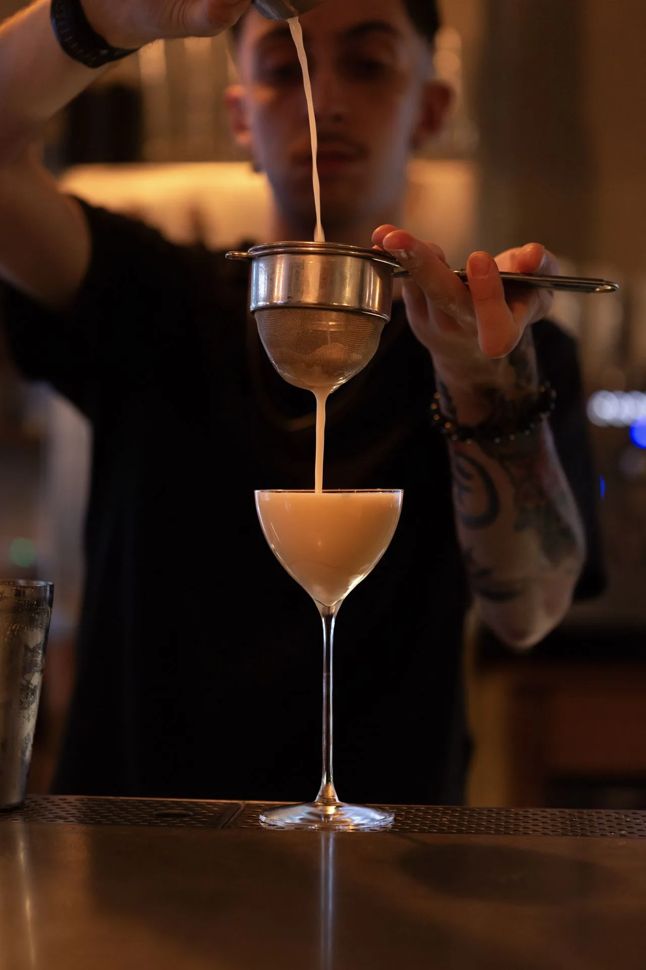 Barman versant un cocktail au chinois dans une coupe, au bar du Café des Délices