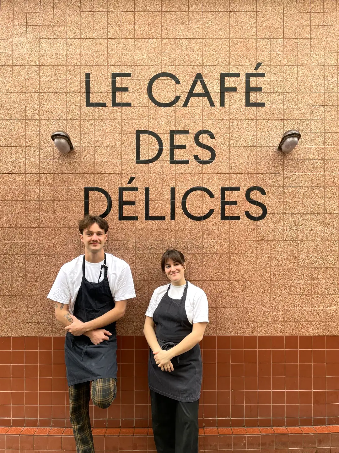 Le chef et la cheffe du Café des Délices devant l'enseigne du café