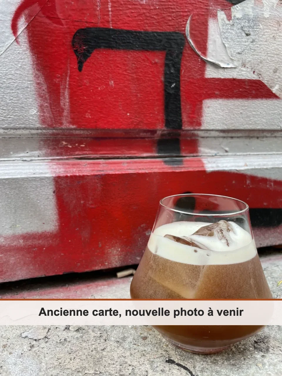Cocktail ambré à la mousse blanche servi en verre tulipe, devant un mur tagué rouge